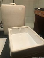 View of storage settee inner compartment with off-white fabric lining, base and sides, and padded removable top base.