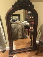 Frontal view of the large arched wooden framed mirror showing its carved decorative top and polished wood finish.