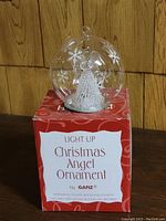 Light Up Christmas Angel Ornament in original box with label showing alternating yellow, red and blue lights and replaceable button-cell batteries.