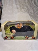Full view of Anne Geddes Baby Butterflies Monarch doll in original box with butterfly decorations and background scene.