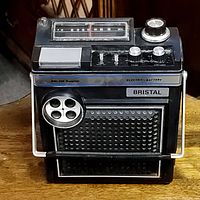 Front and top view of the vintage Bristal AM-FM radio showing speaker grille, tuning scale, control knobs, and carrying handle.