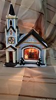 Full view of the ceramic church figurine with lit interior and snow-covered trees at the base