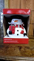 Front view of the snowman cookie jar inside red packaging box with label