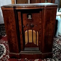 Front of the antique wooden radio cabinet with the doors open, showing the tuning knobs, meter, and speaker grille.