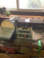 Side view of the Delta sander showing the belt and disc sander setup on a workbench with surrounding tools and supplies.