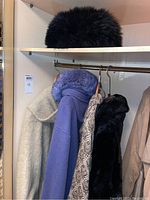 Black fur hat on top shelf, various coats including beige, blue, and patterned car length jackets hanging on a rod.