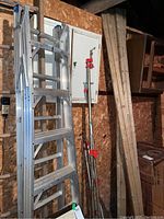 Aluminum extension ladder leaning against the wall with a white panel behind it, wooden planks next to it