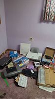 Wide view of lot showing laptop, printers, keyboards, router and boxed Philips BluRay player on carpeted floor.