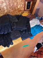 Photo showing multiple pairs of women's leather gloves in black, brown, tan, and white colors on a wooden surface.