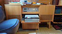 Mid-century modern wooden stereo cabinet with equipment and some household items on top, showing the Philips audio gear inside the cabinet compartments.