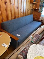 Front and left side view of sofa in paneled room beside rugs and coffee table