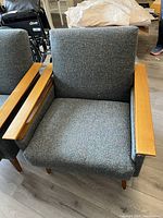 Front view of one chair showing grey multicolor boucle fabric seat and backrest with teak wood arms and legs.