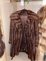 Front view of the brown mink fur coat hanging on a wooden hanger showing the length, collar, and hook closure details.