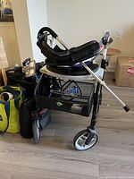 Full side view of foldable walker with padded seat, mesh basket, and one aluminum cane resting on it