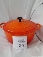 Orange cast iron enamel pot with lid, showing overall exterior condition and color, with seller tag visible