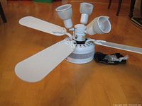 Ceiling fan with white blades and three adjustable light fixtures, shown disassembled on wooden floor.