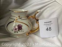 Side view of ceramic vessel showing floral design and elaborate gold plated handle.