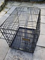 Front angle view of black metal wire dog crate showing door with latch and removable plastic tray inside.