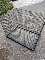 Full view of black metal wire Petmate dog crate with removable tray on pavement outdoor.