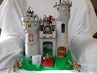 Front view of the gray plastic Fisher Price castle with green base and figures positioned around and on the castle.