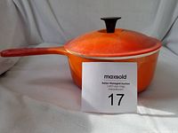 Photo showing orange cast iron enamel pot with lid on, orange handle and black knob on lid, seller card in front.