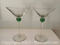 Pair of clear martini glasses with green globes on stems shown side by side against white background.
