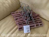 Top view of 10 pink plastic pant hangers stacked together with metal hooks aligned.