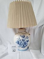 Front view of the table lamp showing the blue floral ceramic base and beige pleated lampshade.