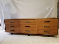 Full front view of teak dresser showing all nine drawers and black handles.