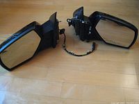 Pair of GMC 1500 power door mirrors with wiring harnesses shown from the mirror glass side on wooden floor.