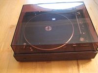 Turntable with closed dust cover showing full exterior with wood base and black top plate.