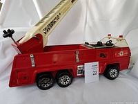 Side view of red and white vintage Tonka firetruck with extending ladder and three pairs of black wheels.