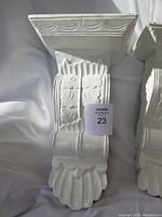 Front view of one white painted wood wall corbel showing carved decorative details and paint texture.