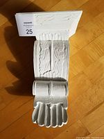Front view of white painted wood corbel with floral carvings and scroll detail on bottom edge, on wood floor background.