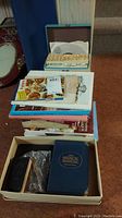 Stack of assorted books including cookbooks and bibles, with a box holding The Merck Manual and some other items