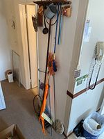 Full view of hallway corner showing antique rake leaning against wall with hanging decorative sunflower flag pole and shepherd's hooks beside it