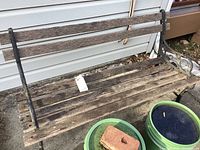 Front view of weathered wooden slat bench with black metal frame, showing seat and backrest slats and metal armrest design.