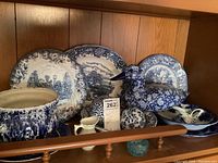 Shelf with various blue and white ceramics including large duck-shaped piece, plates, bowls, and small pitchers.