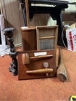 Buttern churn, ornate candlestick, washboard and mallet displayed on carpeted floor against wood-paneled wall