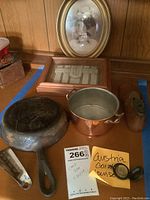 Photo of entire lot showing Griswold cast iron skillet, Austria coin purse, framed beaded bag, framed oval photograph, metal copper pot, wooden shoe form, and metal shoe horn on wooden surface.