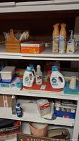 Shelf with laundry detergents, soap, wooden trays, and cleaning supplies.