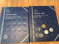 Two blue coin albums labeled for Lincoln Cent collections 1909-1940 and 1941-1974, with several loose coins on top including pennies and steel cents.