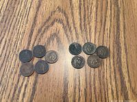 Top-down view of 10 Indian Head pennies spread in two groups on a wooden table, showing various degrees of wear and discoloration.