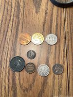 Photo of all eight coins and tokens arranged on wooden surface, showing variety of metal types and designs