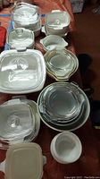 Overview of multiple CorningWare dishes, casseroles and lids alongside Pyrex mixing bowls and a white bowl