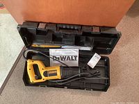 Electric Dewalt reciprocating saw placed inside a black plastic carrying case along with instruction manual and saw blades.