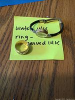 Watch and ring on wooden table next to yellow note reading seller markings