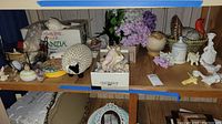 Overview of shelves with assorted shells, figurines, faux flowers, ceramic turkey, wire basket, and assorted ceramic items.