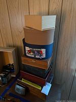 Stack of assorted storage boxes of various materials and designs, including wooden and fabric covered boxes, and a men's leather wallet at the base.