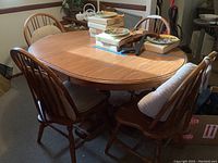 Oak dining table with 12 inch leaf inserted and four matching chairs around it. Worn surfaces with some tape residue visible, various items placed on table.